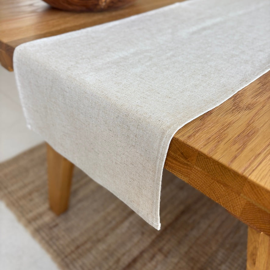 Image shows folded beige table runner on a set dining table. Hand-woven from 100% sustainable French linen, this table runner adds an earthy elegance and style to your dining table. Dimensions: 220cm x 30cm
