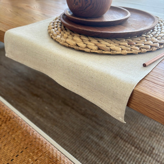 Image shows folded beige table runner on a set dining table. Hand-woven from 100% sustainable French linen, this table runner adds an earthy elegance and style to your dining table. Dimensions - 110cm x 40cm