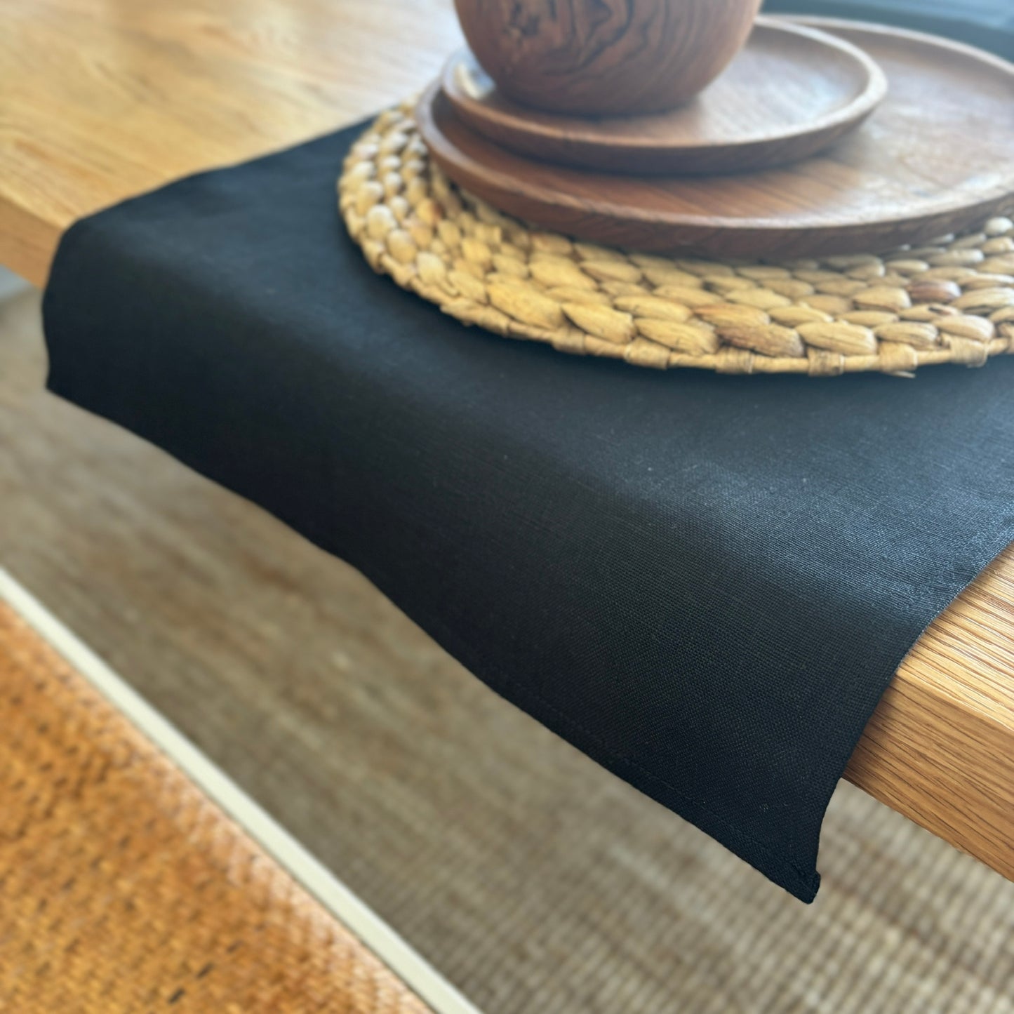 Image shows folded black table runner on a set dining table. Hand-woven from 100% sustainable French linen, this table runner adds an earthy elegance and style to your dining table. Dimensions - 110cm x 40cm