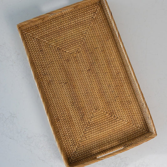 A rectangular woven rattan tray with integrated handles, shown from an overhead angle on a light gray textured surface.