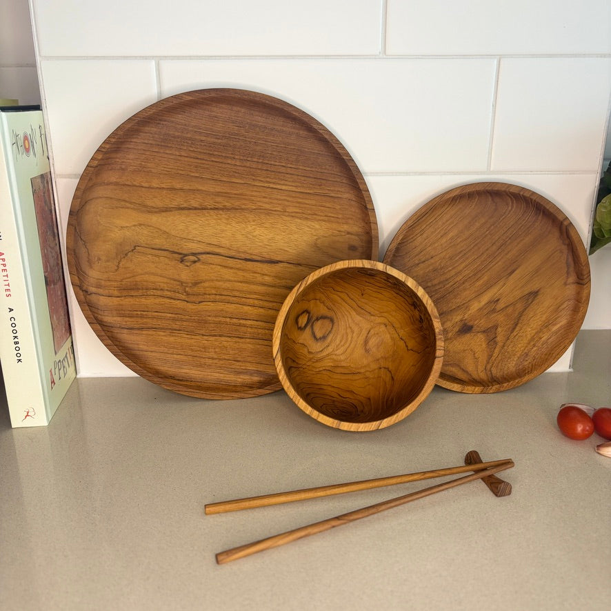 Images shows a stunning trio of handcrafted pieces, comprising a larger plate (28cm x 2cm), smaller plate (20cm x 1.5cm) and a bowl (14cm x 8cm). All pieces are handcrafted from sustainable teak and are as durable as they are stylish.