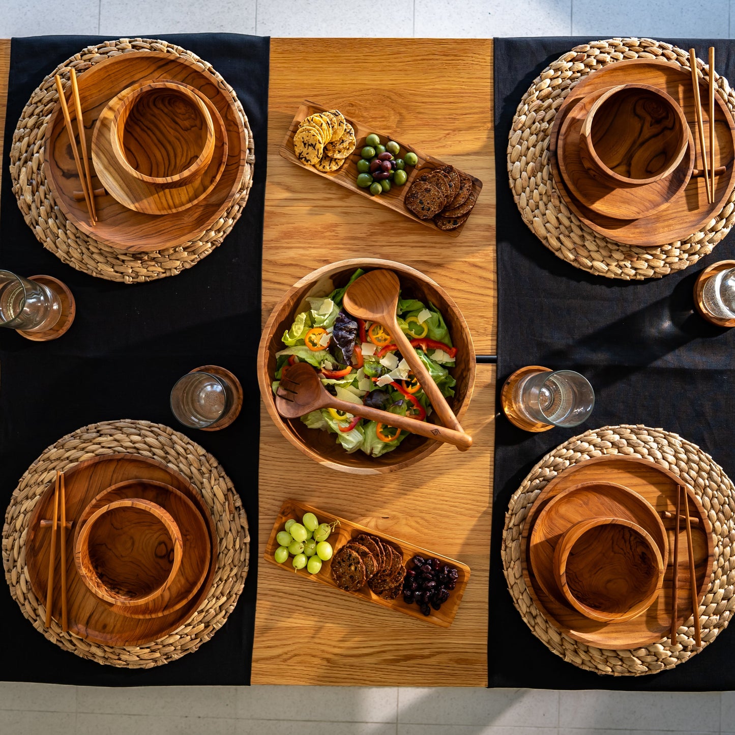 Single piece teak salad serving bowl with 2 serving utensils on a clean dining table setting