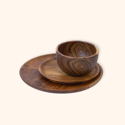 A dark grained grained teak wooden bowl, sitting on a small plate and stacked on a round wooden plate, all featuring a prominent natural wood grain pattern, set against a solid off-white background.