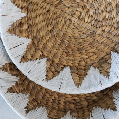A close-up of a water hyacinth woven round basket, featuring a white braided starburst border around the edge.