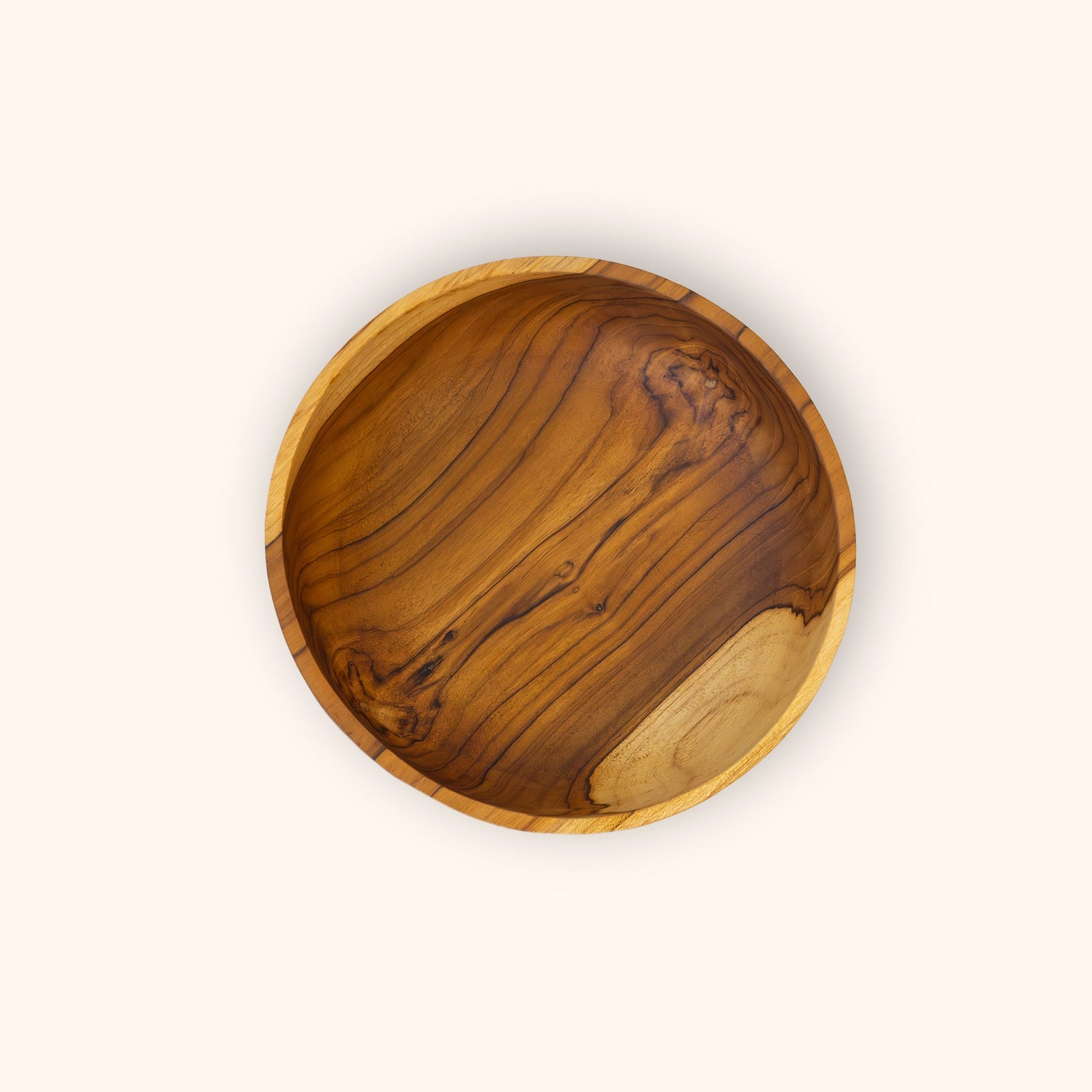 A round teak wooden bowl with a rich grain pattern, photographed from directly above on a solid off-white background.