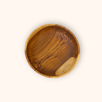 A round teak wooden bowl with a rich grain pattern, photographed from directly above on a solid off-white background.