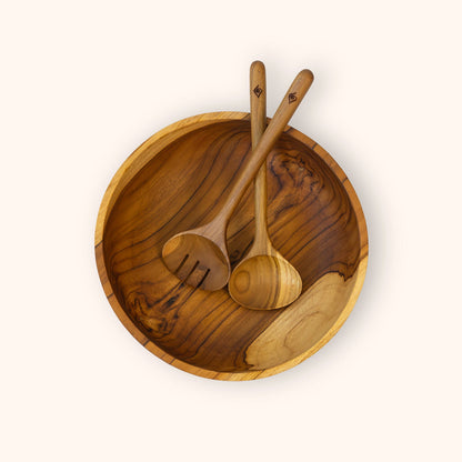 A round wooden salad bowl with two wooden salad serving spoons resting inside, photographed from above on a plain off-white background.