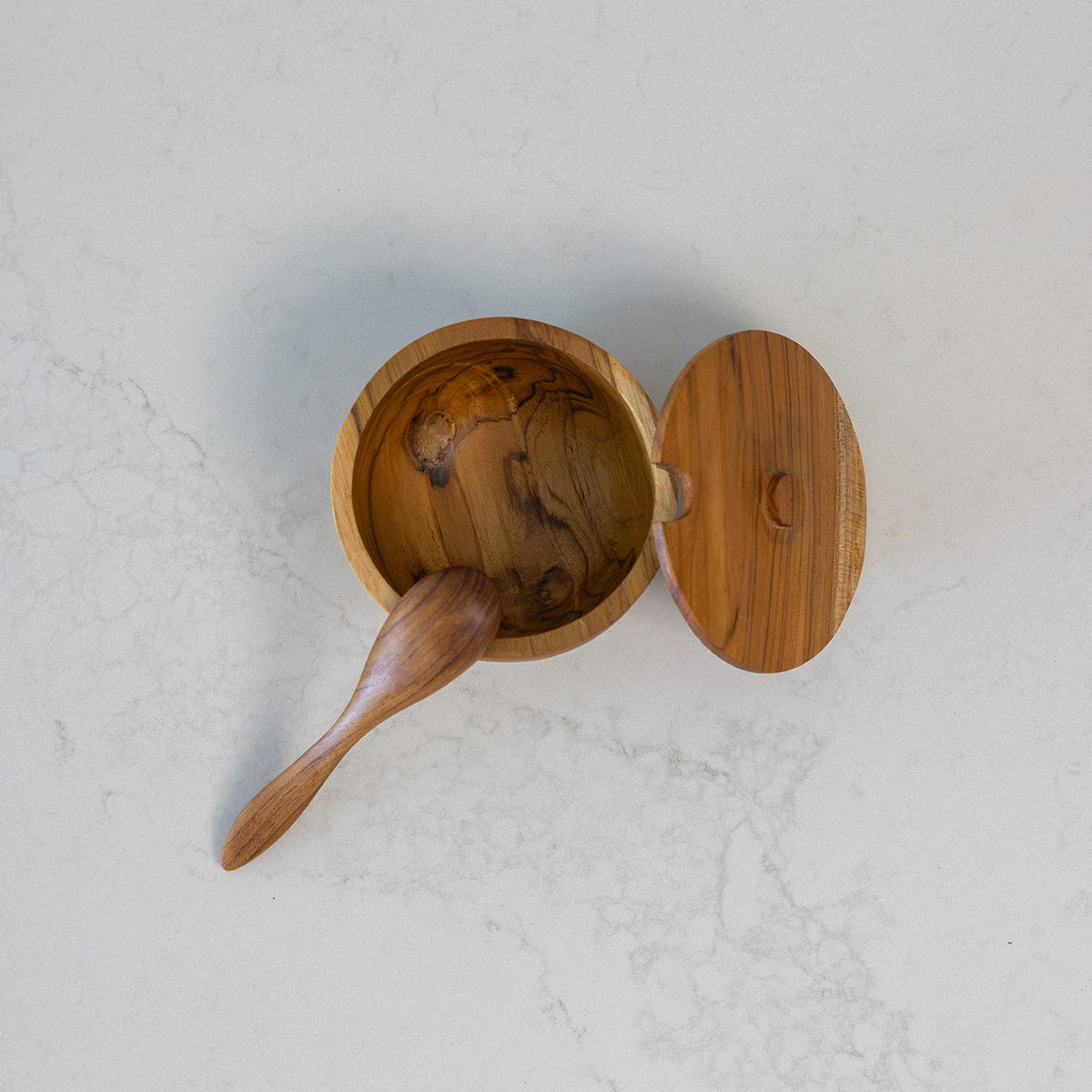 Teak salt keeper with spoon shown on a clean marble bench from overhead angle