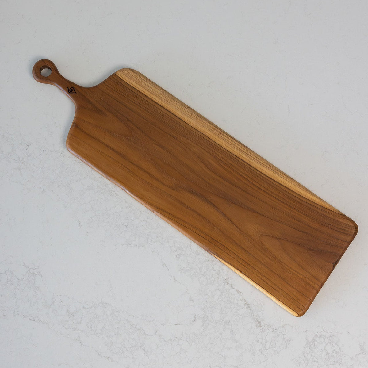 A rectangular wooden serving board with rounded corners, a built-in handle loop, and a contrasting light wood edge, photographed on a light stone-textured surface.
