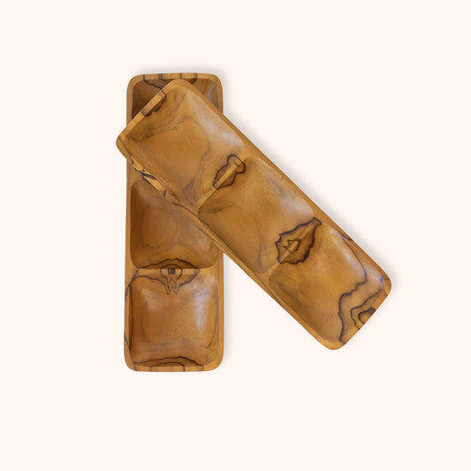 Two rectangular wooden trays with three separate carve-outs for snacks, with glossy finish and natural grain patterns, one standing vertically and the other lying diagonally on top, set against a solid off-white background.