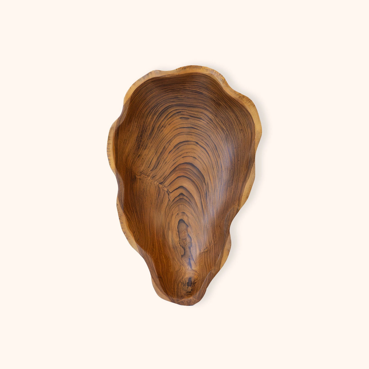 A handcrafted, organic-shaped, teak wooden bowl with a rich brown wood grain pattern, photographed from directly above on a solid cream background.