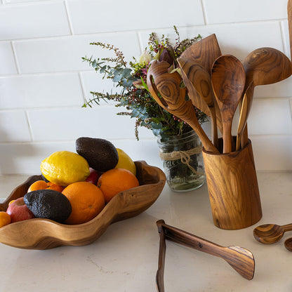 A collection of hand-crafted teak wooden utensils and beautiful organic-shaped teak bowl with ripe oragnes, lemons and avacados in it. 