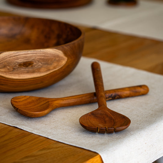 Image of teak salad bowl with a pair of teak salad servers. Durable and high quality, handcrafted from sustainable teak root, which makes every piece a one-of-a-kind.Dimensions 28cm x 9cm x 2cm.